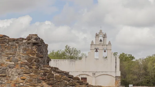 White frescoed church with a stone ruin to the left in the foreground.