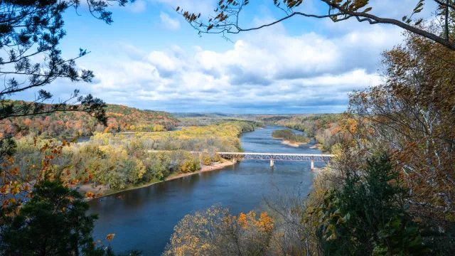 A blue river winds through a valley lined with trees in autumn color.