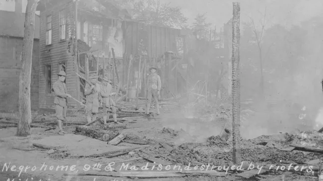 Historic photo of militia members standing in the remains of a burned building.