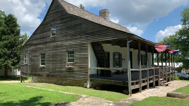 Frame house made of wood with U.S. and French flags flying on front porch.