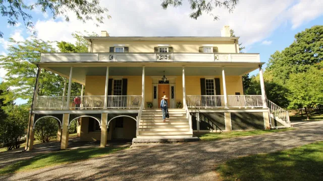 A three story house with large porch across the front and flight of steps leading to the ground.