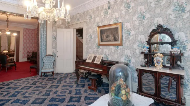 A Victorian-era parlor with blue wallpaper and blue carpeting.