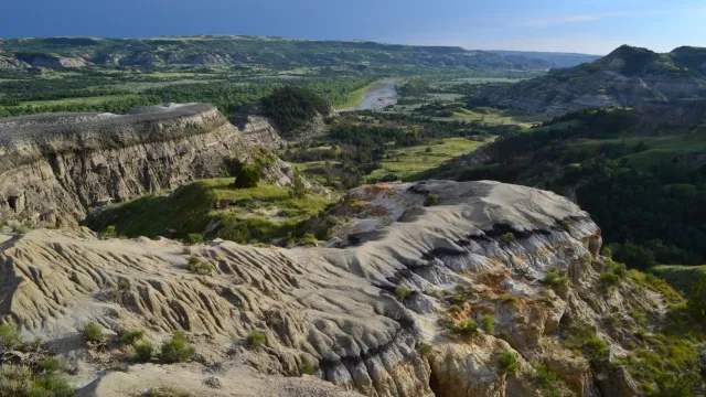 A colorfully striped butte in the foreground overlooks a dark green badlands landscape