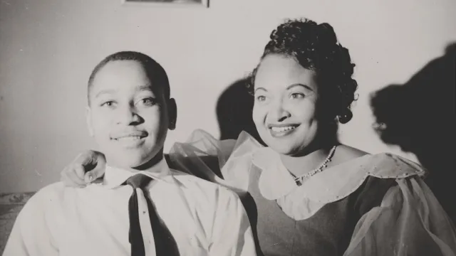 Two African Americans sitting in a room and smiling toward the camera.