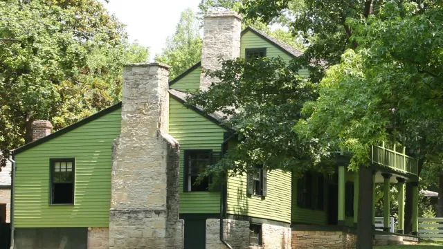 Green sided, two story house with green trees