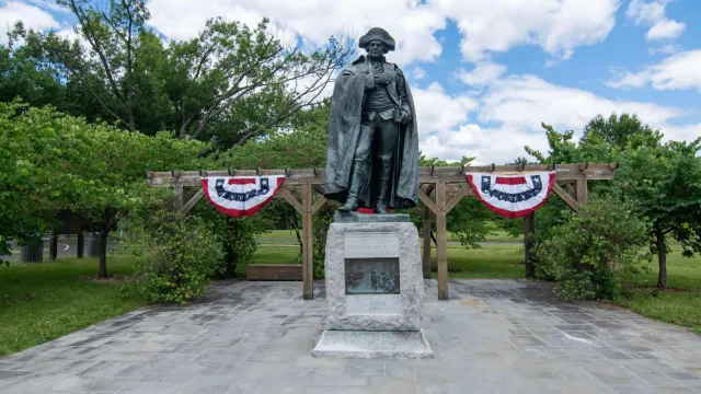 bronze statue of rev war general on stone base, red white and blue bunting behind