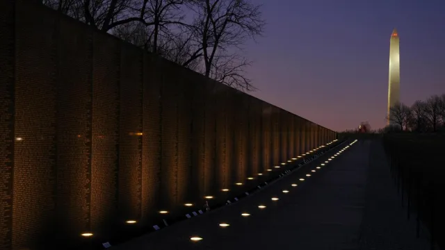 Lights glow at the base of the wall of the Vietnam Veterans Memorial with Washington Monument.