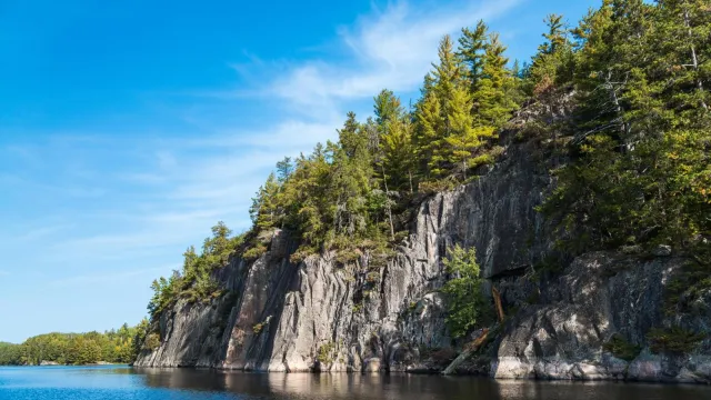 Photograph of granite cliffs topped with trees alongside a blue lake.