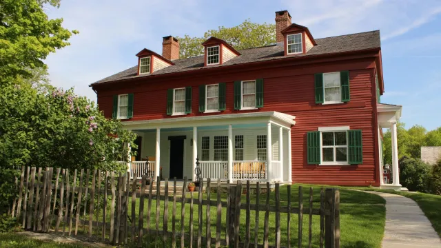 A view of the south side of the Weir House with porch visable, showing a fence in front of the home