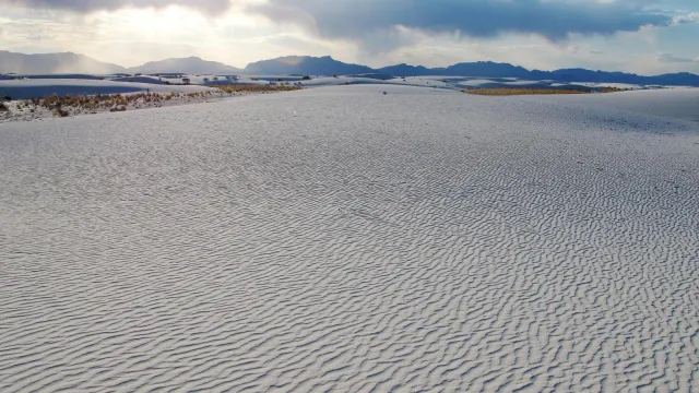 White dunes in foreground with sun setting behind mountain.