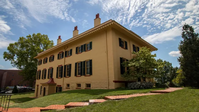 A yellow two-story brick building with tall windows and green shutters on them