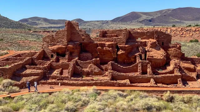 a large stone pueblo in a desert beneath mostly sunny skies with mountains in background